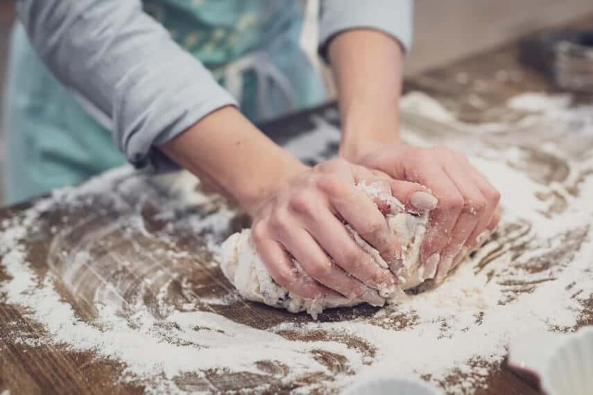 Hands kneading a bread dough on a floured wooded hopping board