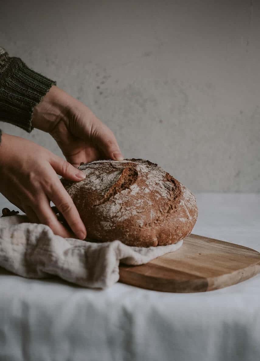 Hands placing a round bread roll on a wooden chopping board