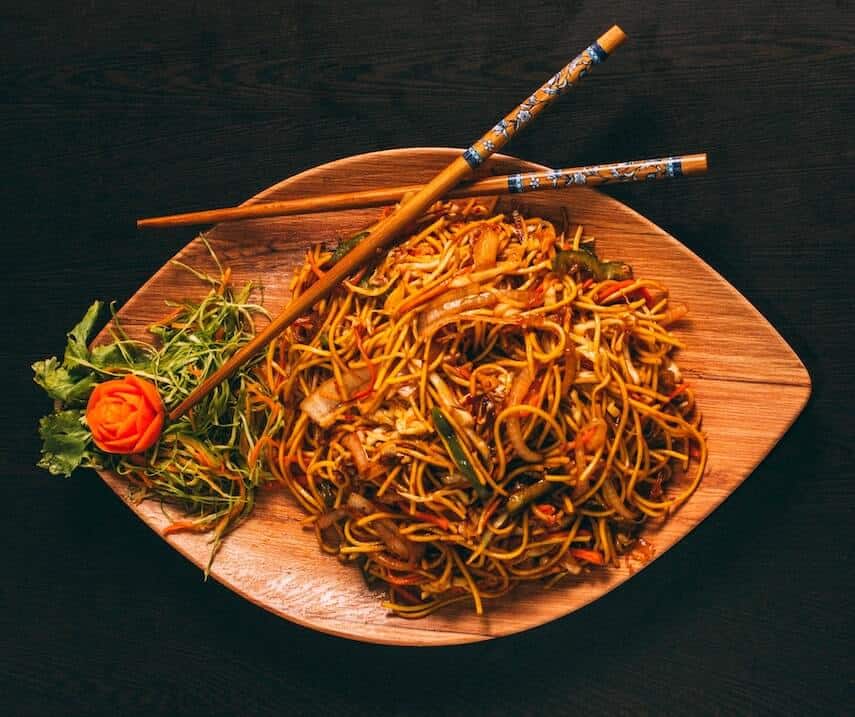 Noodles on an oval shaped wooden bowl with chopsticks crossed at the top