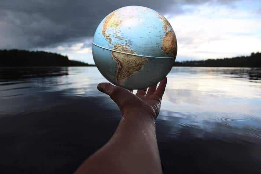 Outstretched hand holding a globe in front of a lake
