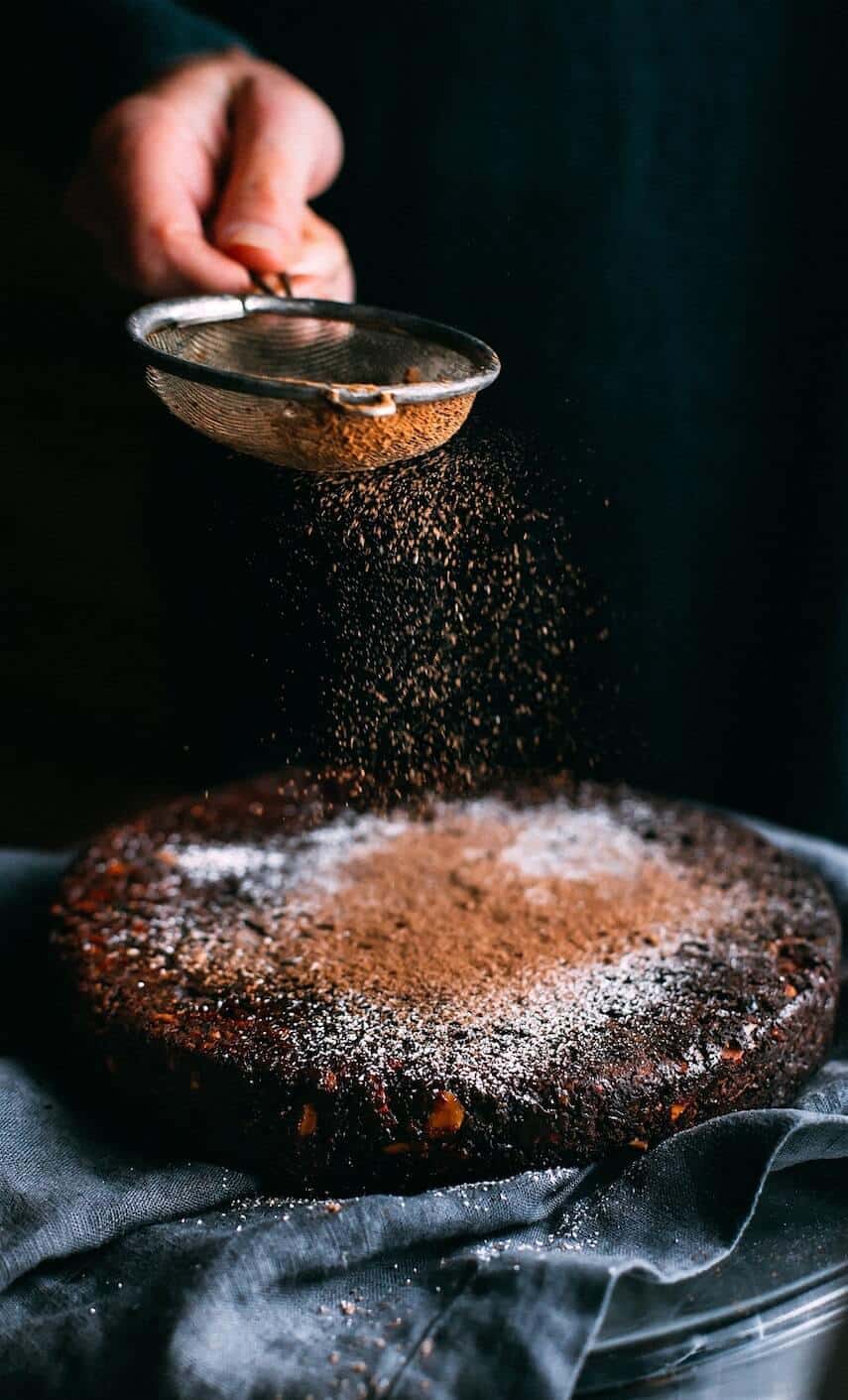 Powdered chocolate being sifted onto a round chocolate cake
