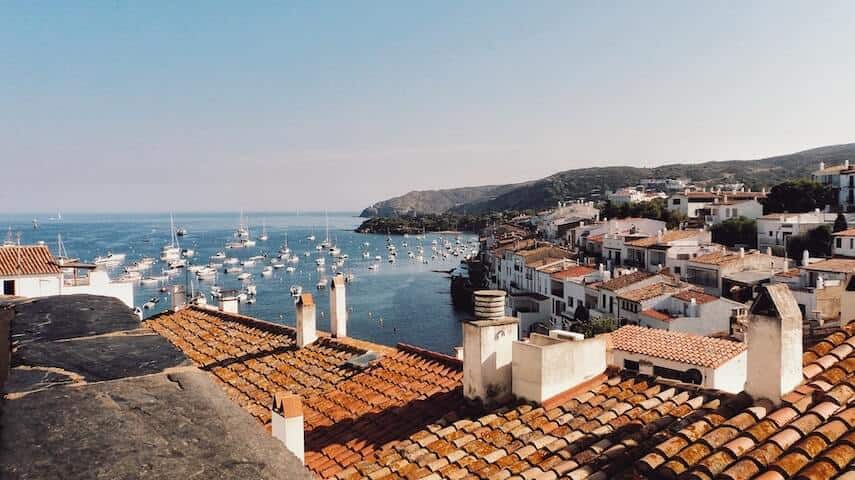 Terracotta roofs and white washed houses on the coast, loats of white boats in the water