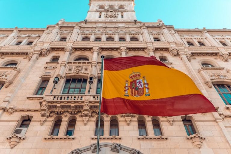 Spain Quiz Questions and Answers cover photo of a beige building with a Spanish flag flying in front