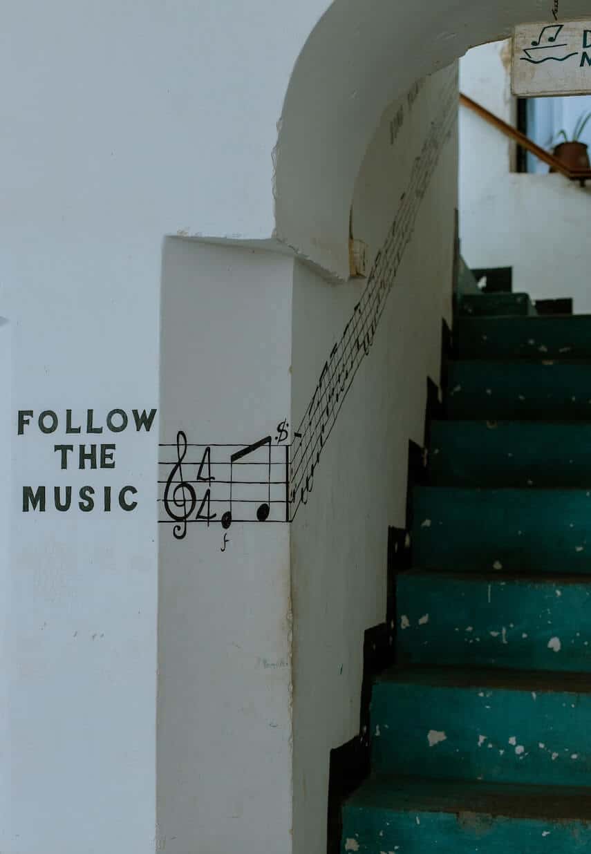White wall next to blue stairs with -follow the music- and a line of notes leading up the wall of staircase