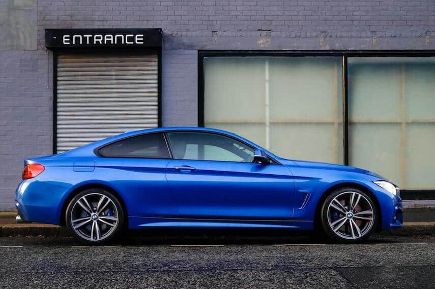 Blue two door coupe BMW car parked in front of a store with empty windows and a rollerdoor with the word Entrance over the top
