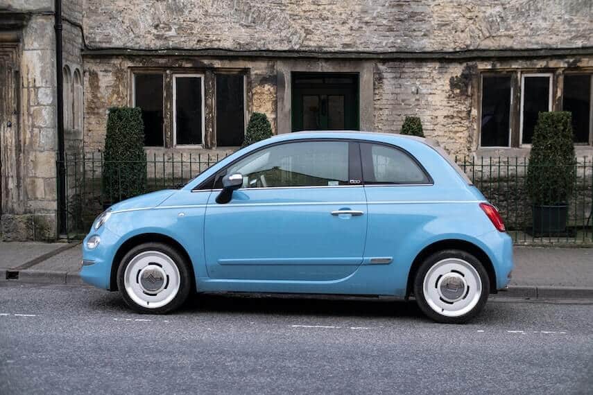 Light blue Fiat 500 parked in front of an old stone built house
