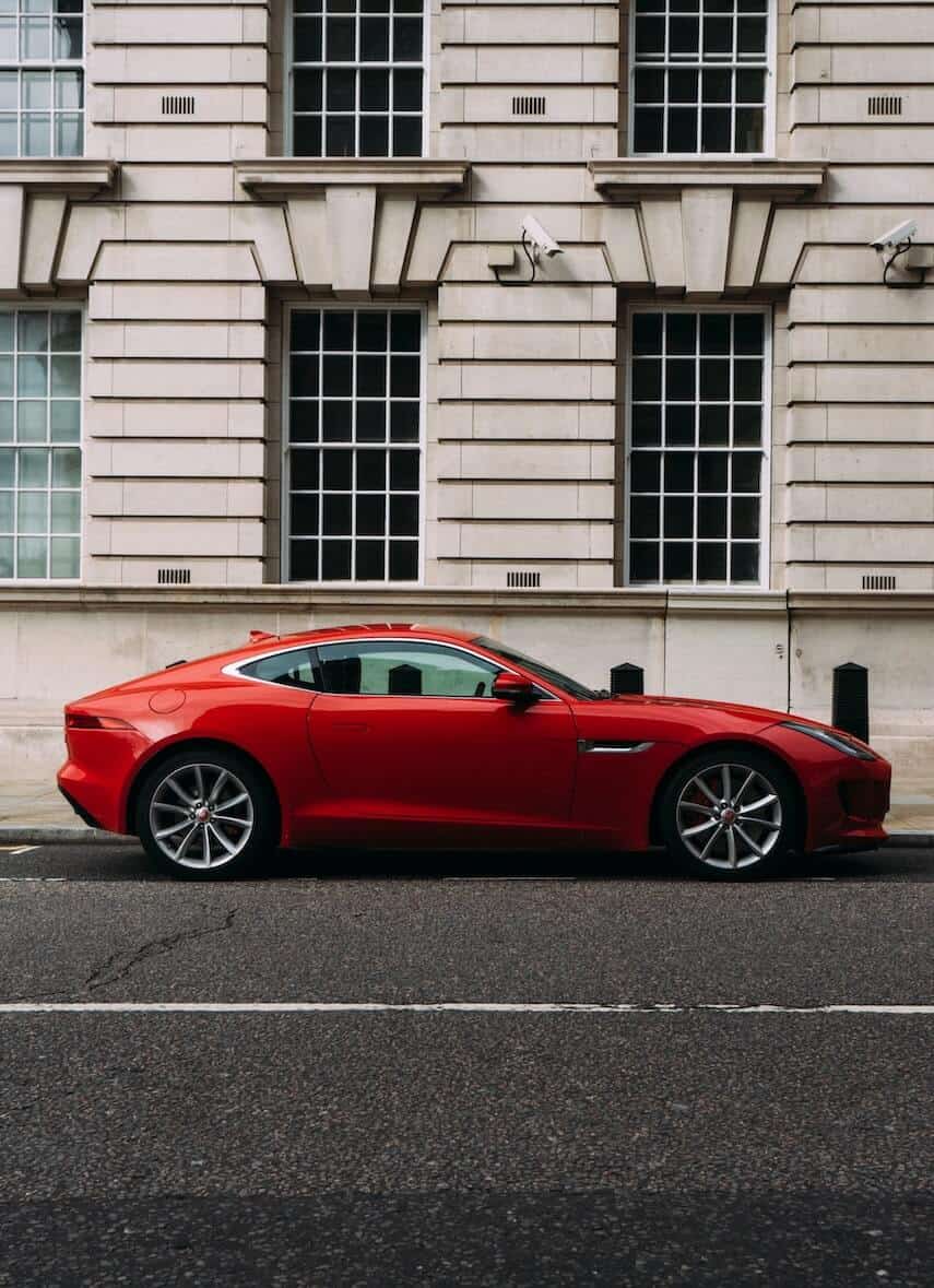 Red 2 door Jaguar sports car parked next to a white stone building in London