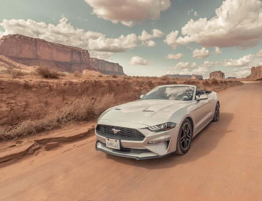 Silver mustang convertible, top down, driving through the red roads and rocky outcrops in Monument Valley National Park