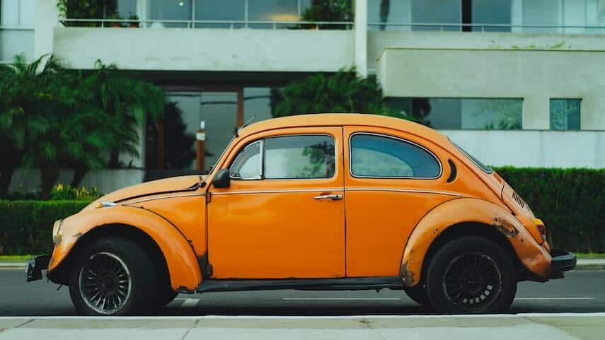 Vintage, rusted orange beetle car parked in front of an apartment building