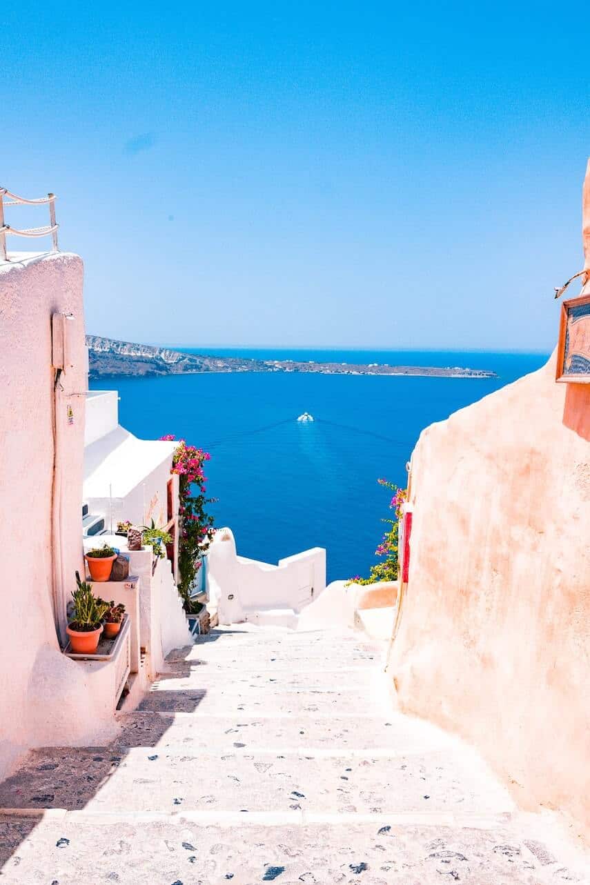 Whitewashed steps between buildings leading down to the deep blue ocean in Greece