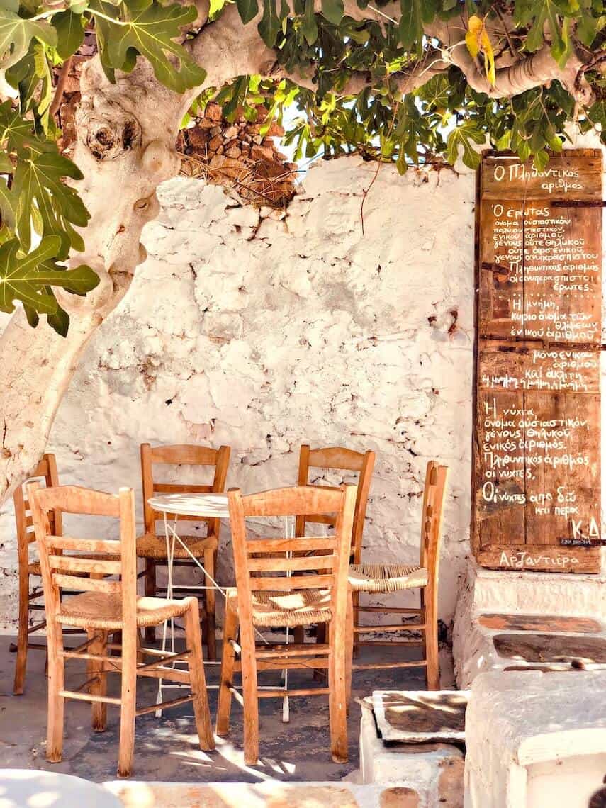 Wooden table and chirs under an old tree, a wooden handwritten menu on the wall next to it