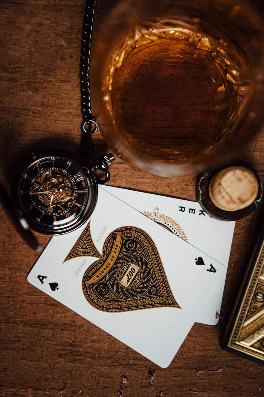 Top down shot of a tumbler of whisky, a pocketwatch, and ace of spades 007 playing cards