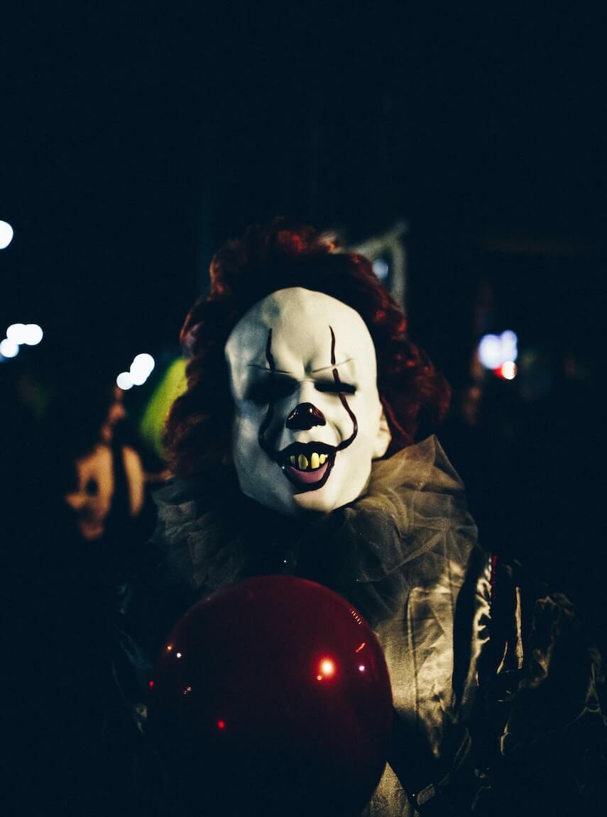 Creepy clown with white face, red hair and carrying a red balloon