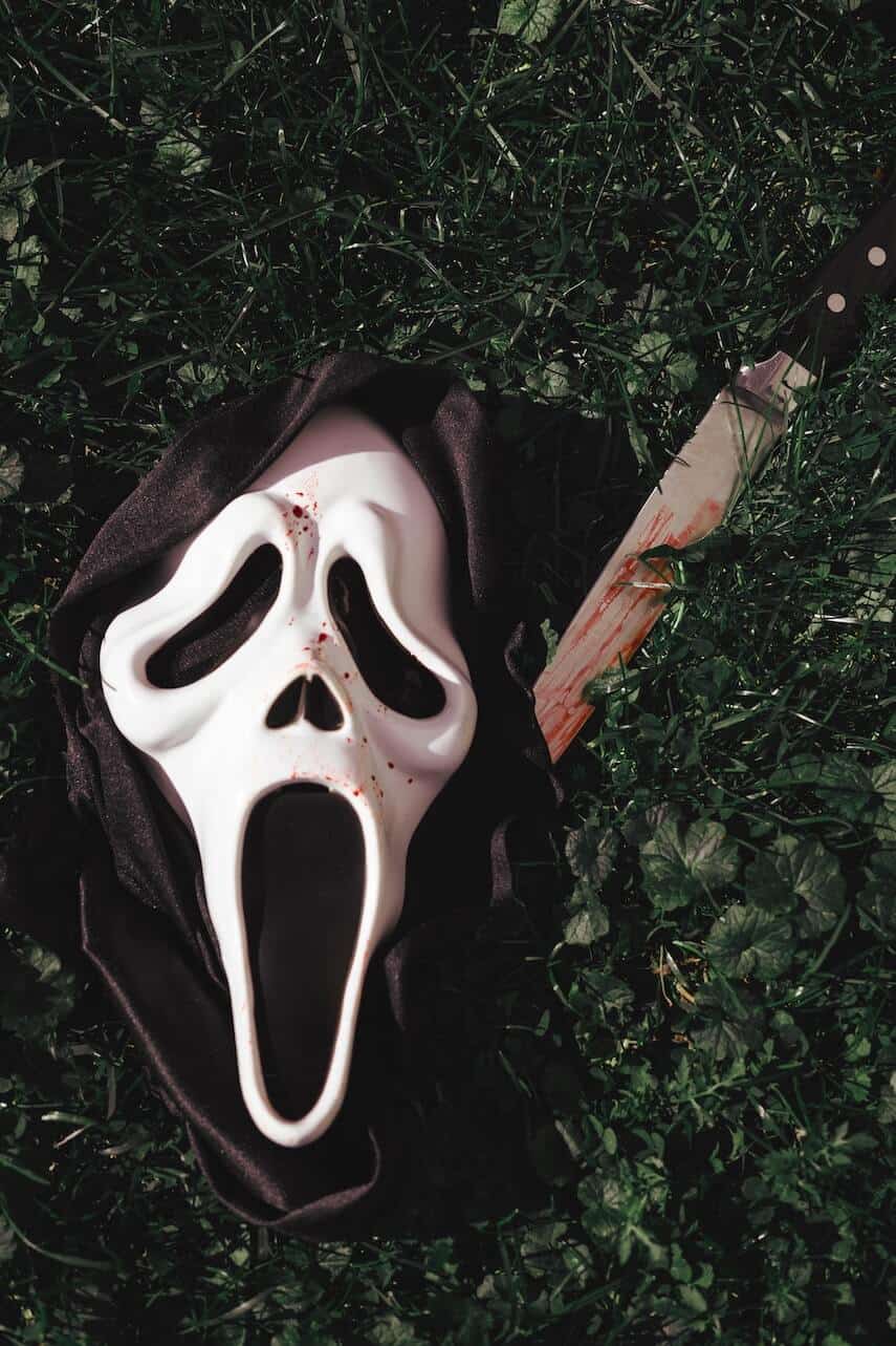 Ghostface scream mask in a black hood, a bloody knife next to it