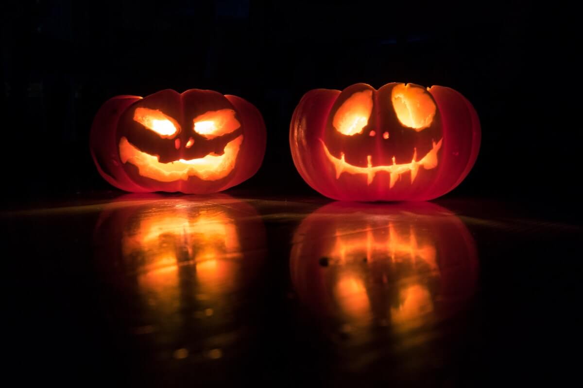 Halloween Trivia Questions and Answers cover photo of two carved pumpkins, lit up from the inside on a black table and in front of a black wall