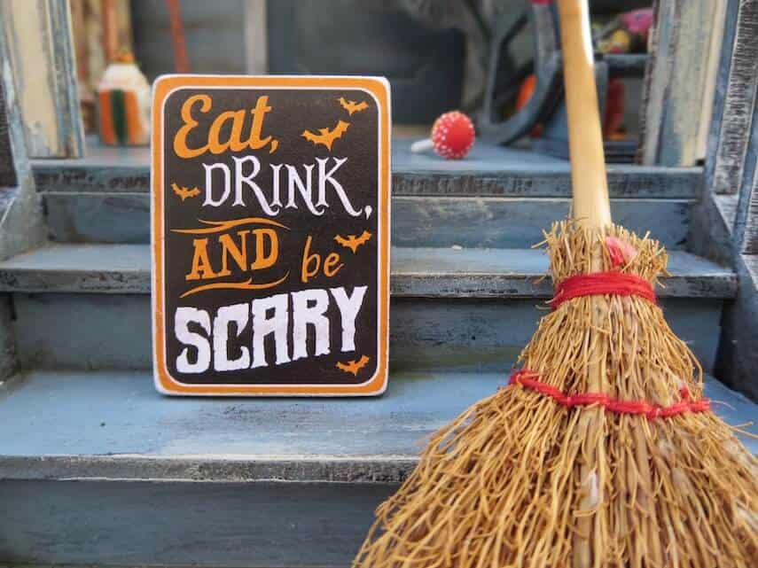 Halloween sign on a doorstep next to a broom with the words 'Eat, Drink and be Scary'