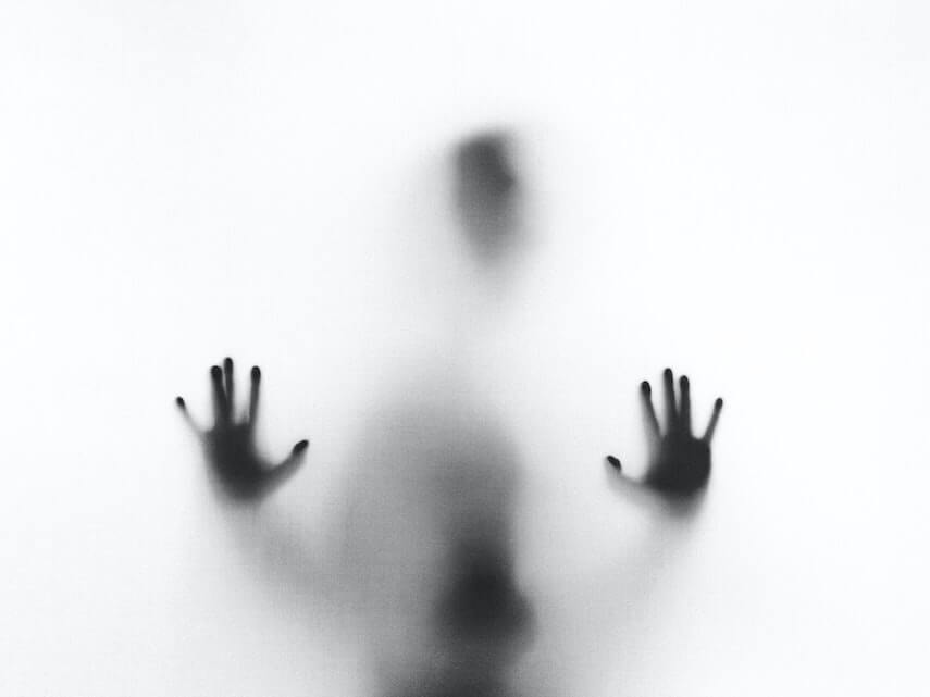 Man standing as a shadow behind a white translucent window, his hands making shapes on the glass