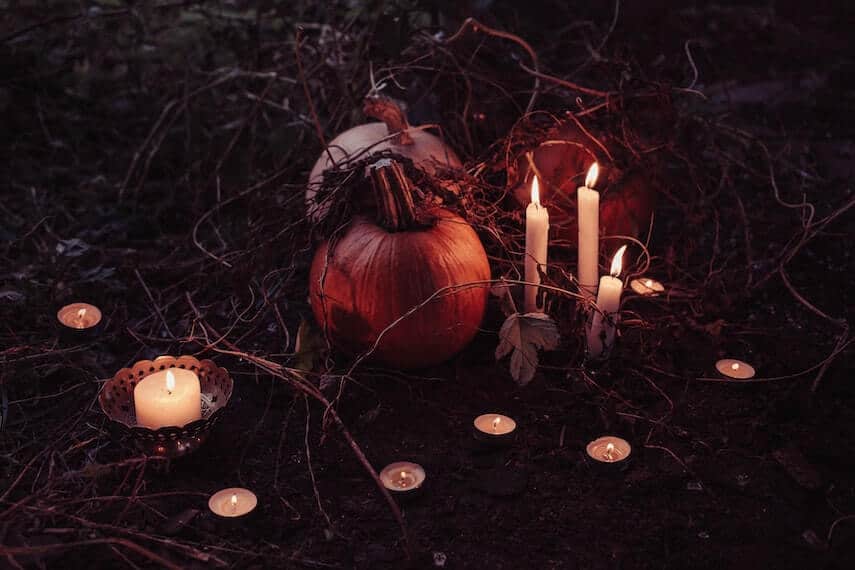 Three small pumpkins surrouded by dried vines and leaves and lit tealight candles