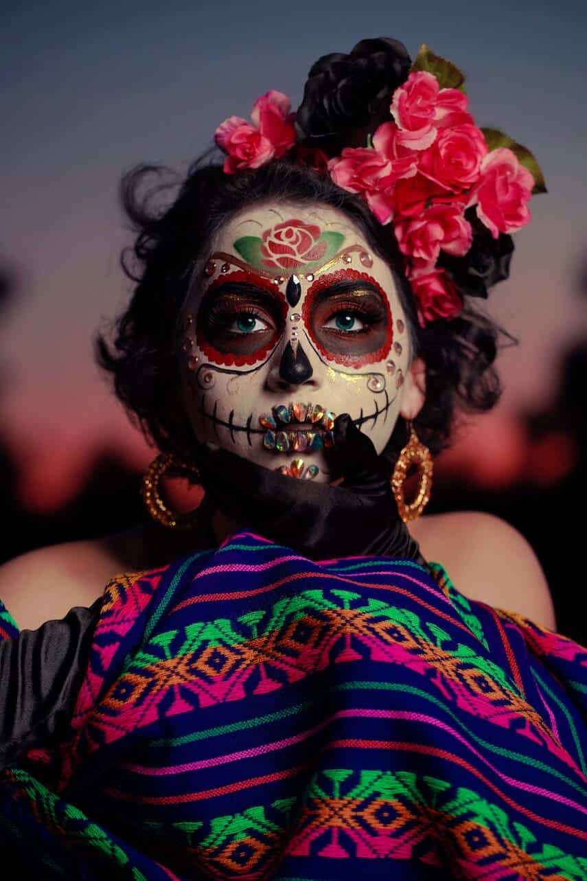 Woman wearing sugar skull style make up, with jewels on her lips and red flowers in her black hair