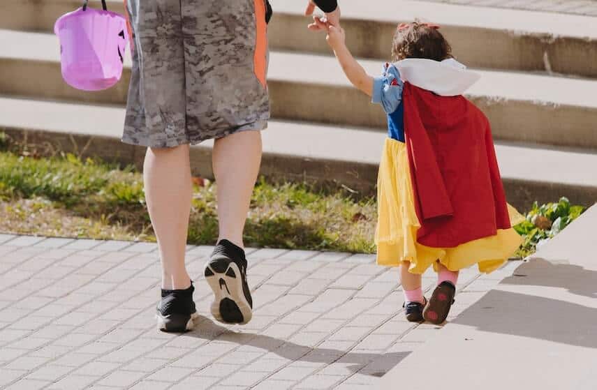 Womans legs and arm reaching down to hold the hand of a small child dressed a Snow White, facing away from the camera